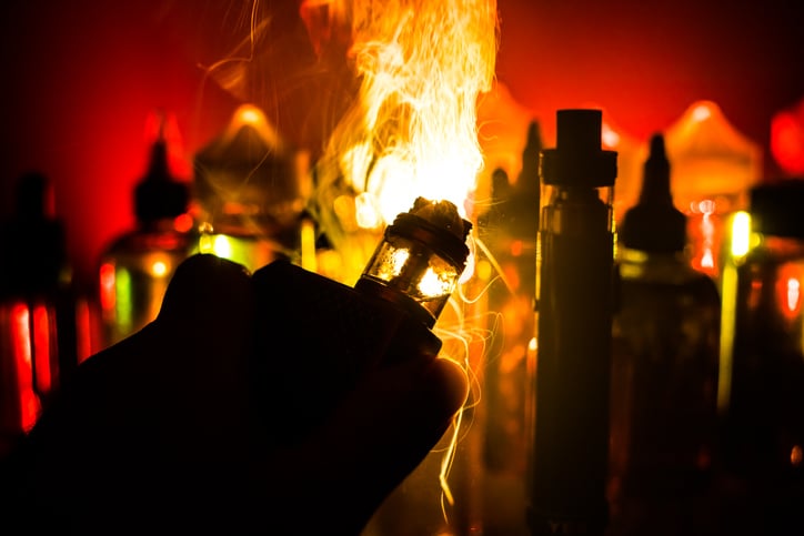 Electronic Cigarette vape explosion. Smoke clouds and vape liquid bottles on dark background. Light effects.