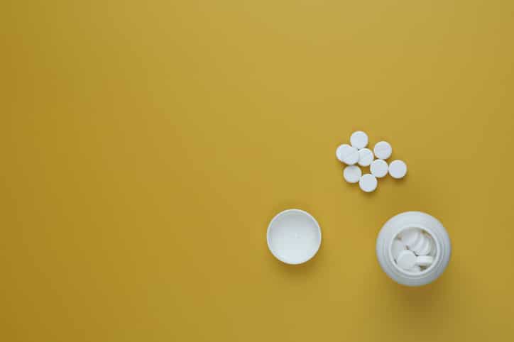 Pill bottle spilling pills on to surface isolated on a yellow background. Copy space. Flat lay.