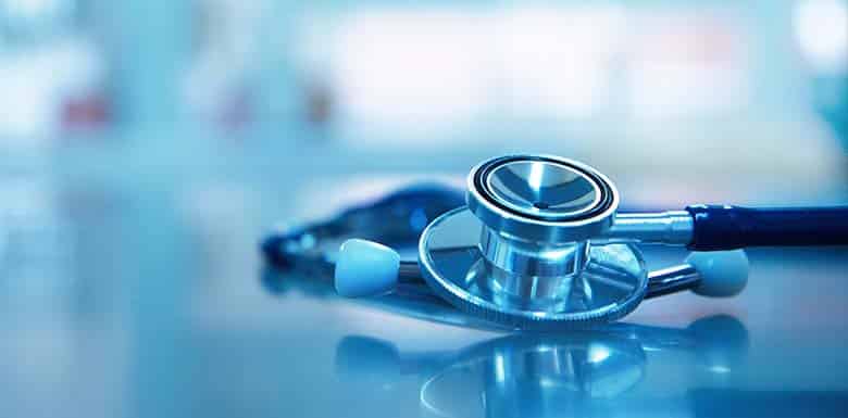 Close-up of a stethoscope on a reflective surface, with a blurred blue and white background.
