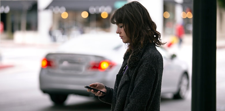 Young woman standing near street with cars in the background waiting for ride to pick her up