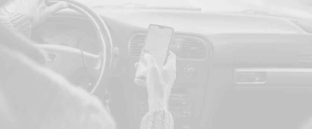 A person holding a smartphone while driving, with one hand on the steering wheel and the other on the phone screen.