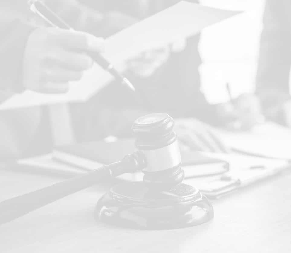 Gavel on a table with people in the background holding documents and taking notes.