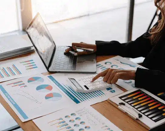 Person working at a desk with a laptop, calculator, and various financial charts and graphs spread out on the table.